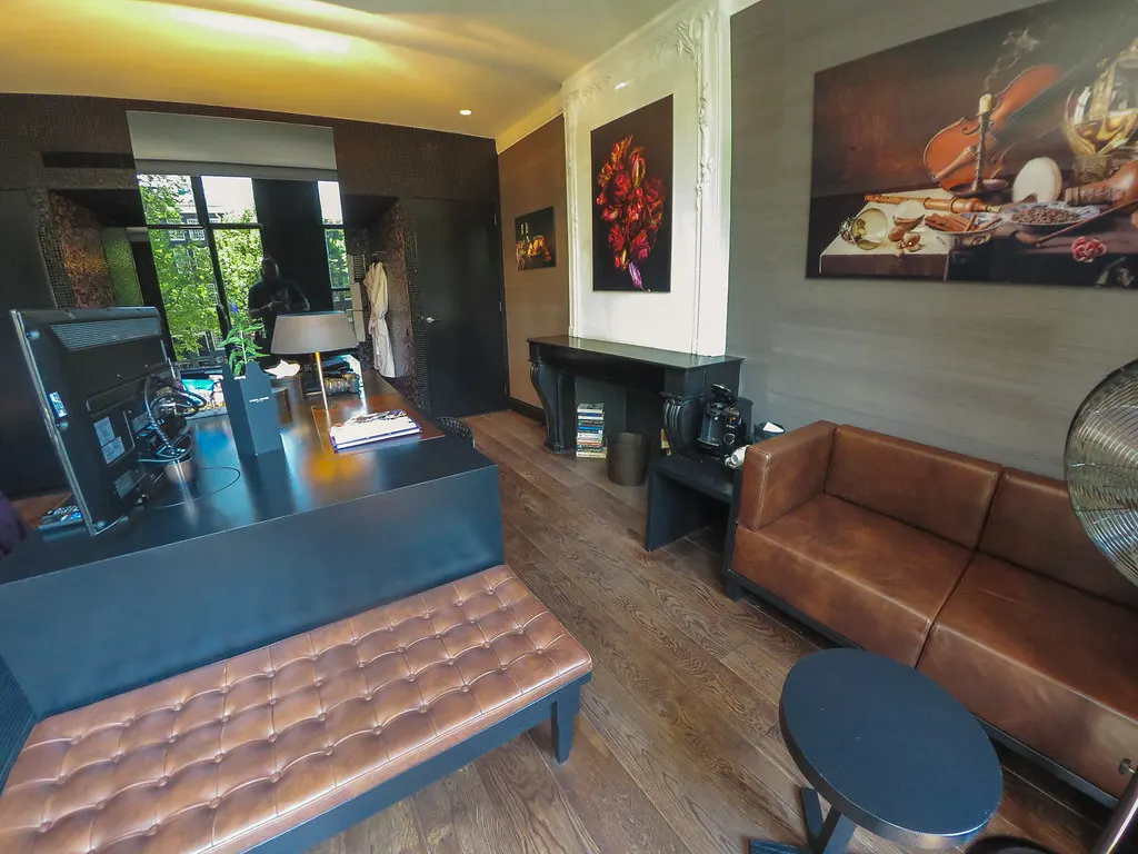 Stijlvolle hotelkamer met donkere houten vloer, bruine leren bank, kunst aan de muur en een bureau bij het raam