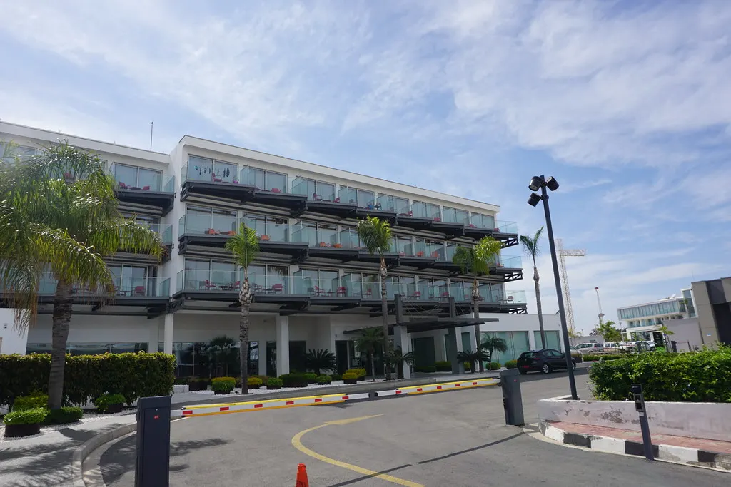 Modern hotelgebouw met balkons, palmbomen en oprit onder een blauwe lucht in Ayia Napa