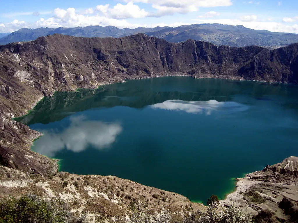 Het groenblauwe kratermeer Quilotoa met weerspiegelde wolken, omringd door steile kraterwanden