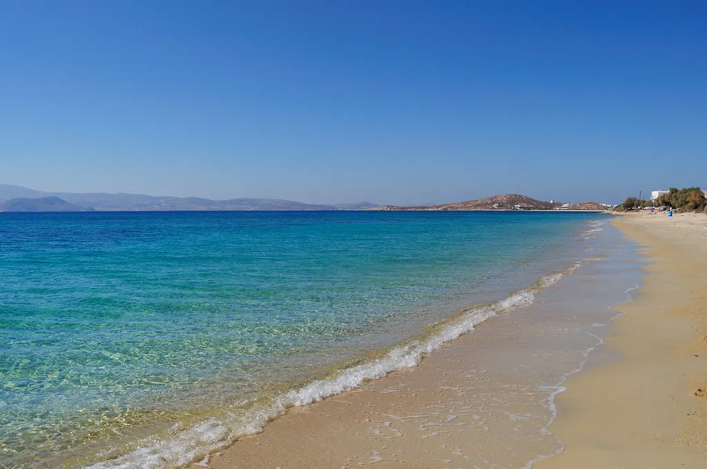 Lang zandstrand met helder turquoise water en heuvels aan de horizon op Naxos