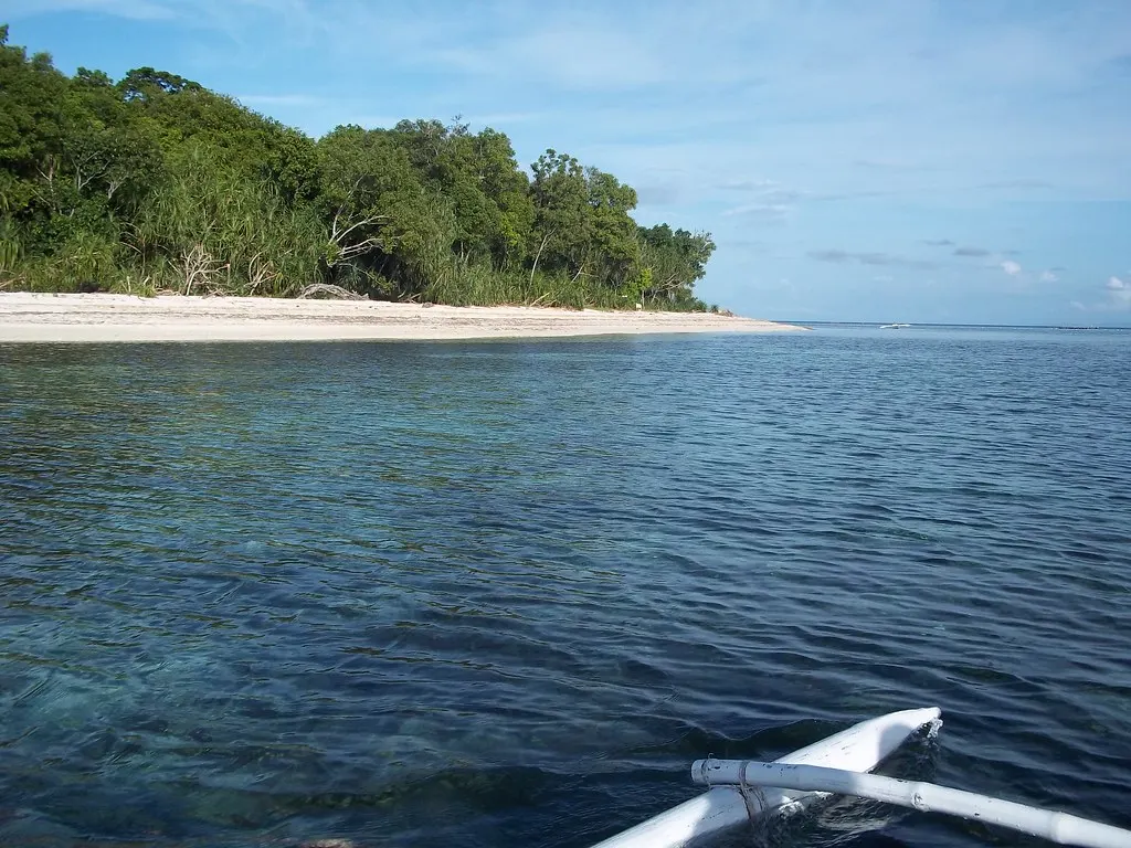 Wit zandstrand en groen bos van Mantigue Island, gezien vanaf een bangka op helder blauw water
