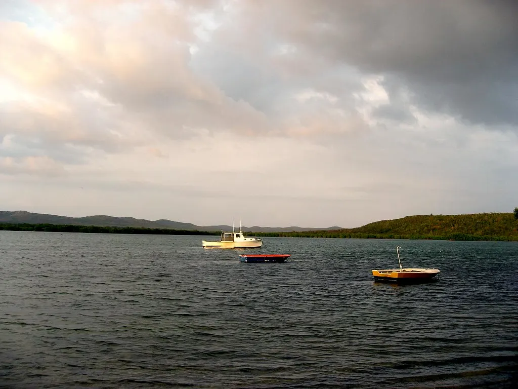 Kalme baai met drie kleine bootjes op het water, omringd door groene heuvels onder een bewolkte avondlucht