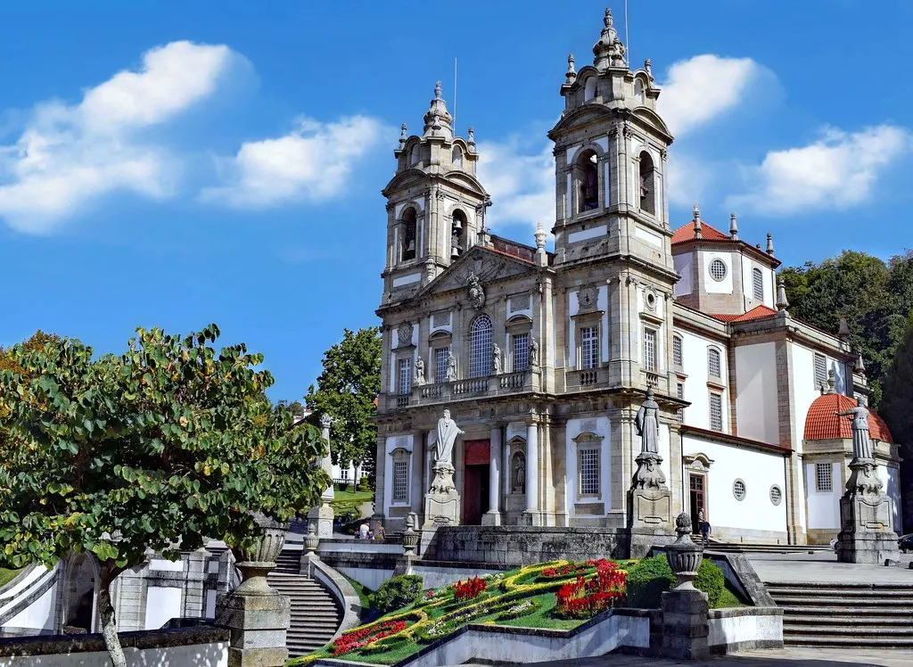 Witte barokke kerk van Bom Jesus do Monte met twee torens, trappen en bloemperk onder blauwe lucht