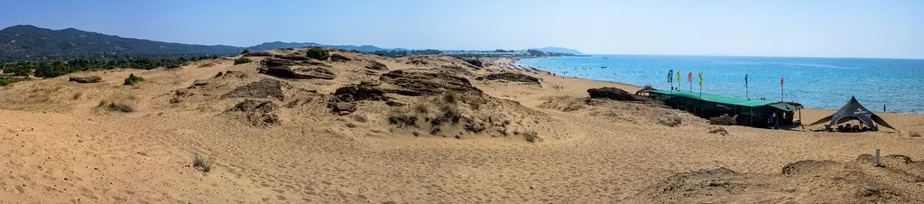 Panorama van zandduinen bij Issos strand op Corfu met blauwe zee en een strandtentje