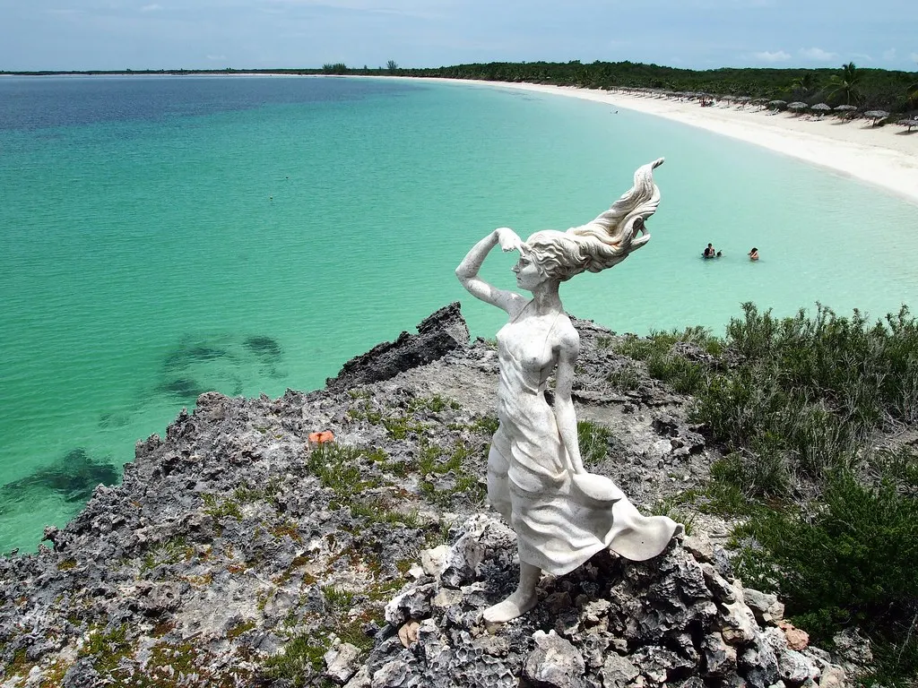 Wit beeld van een vrouw op rotsen boven turquoise zee en wit zandstrand bij Cayo Las Brujas