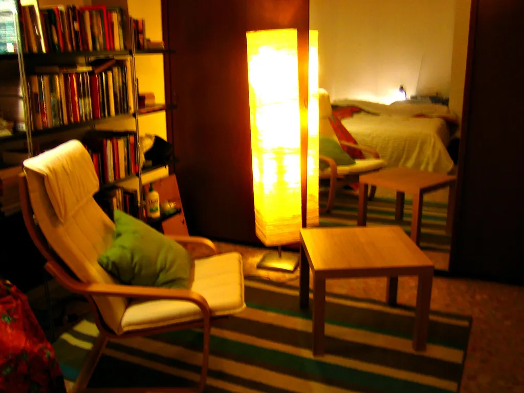 Gezellige appartementwoonkamer met fauteuil, staande lamp, boekenkast en doorkijk naar de slaapkamer