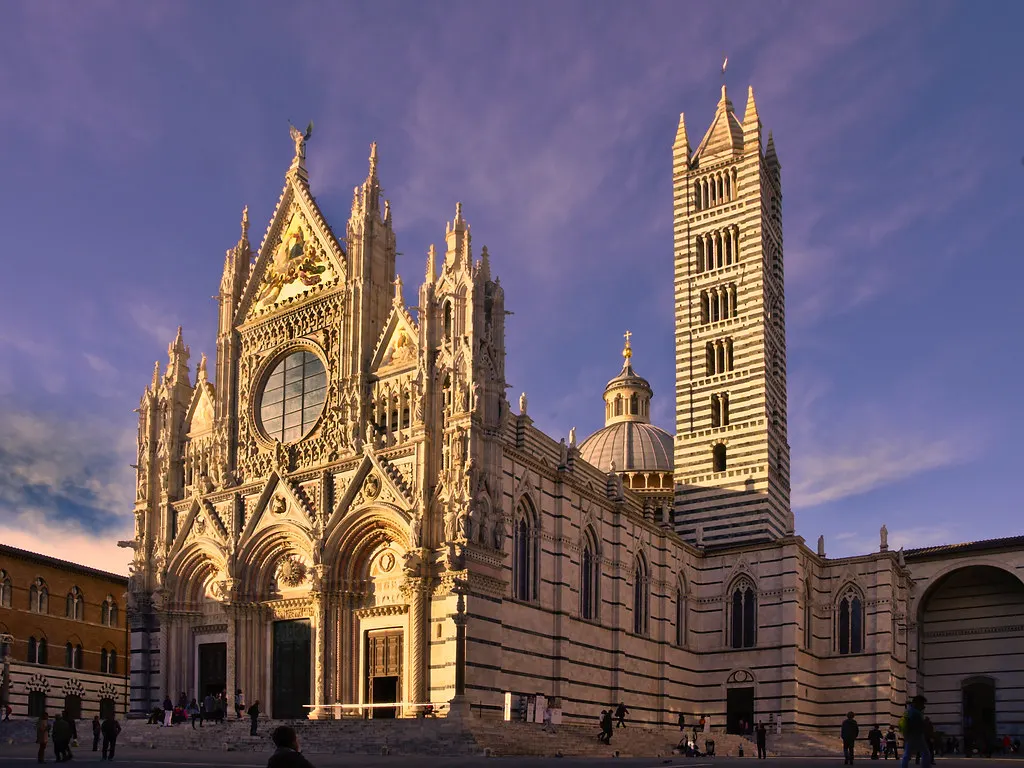 Gotische marmeren gevel en gestreepte klokkentoren van de Kathedraal van Siena in warm avondlicht