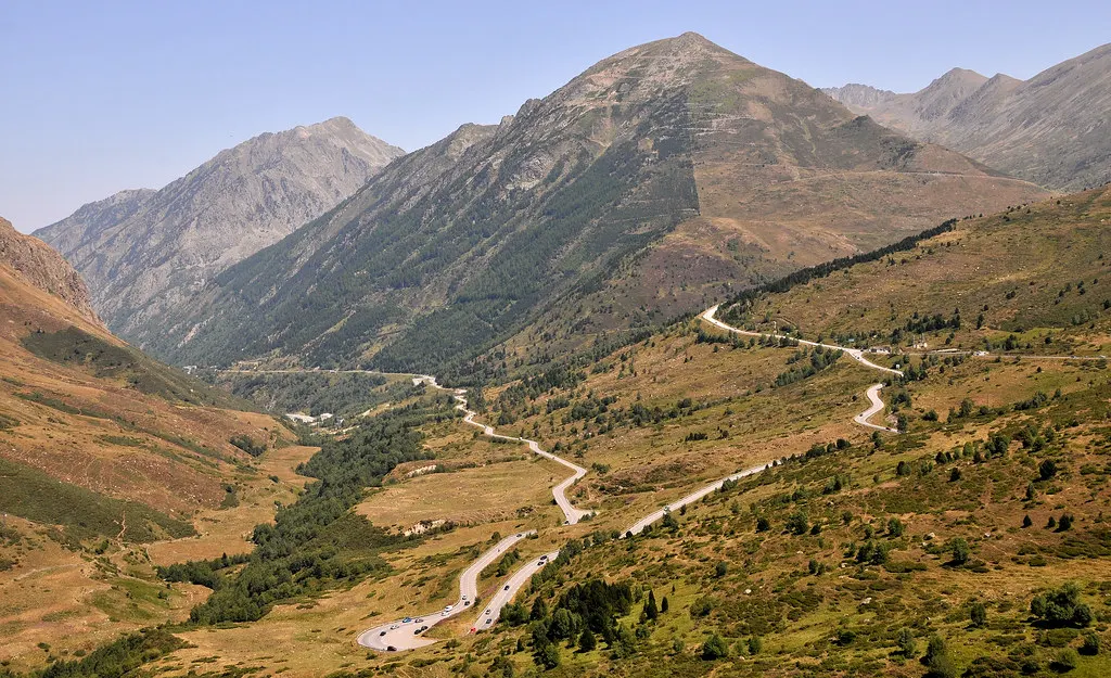 Kronkelende bergweg met haarspeldbochten door een groen-bruin dal in de Pyreneeën