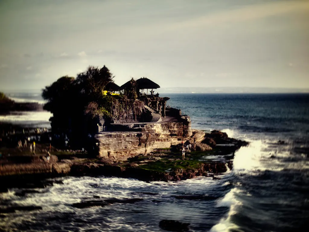 Tempel Tanah Lot op een rots in zee met golven en de rotskust bij zonsondergang