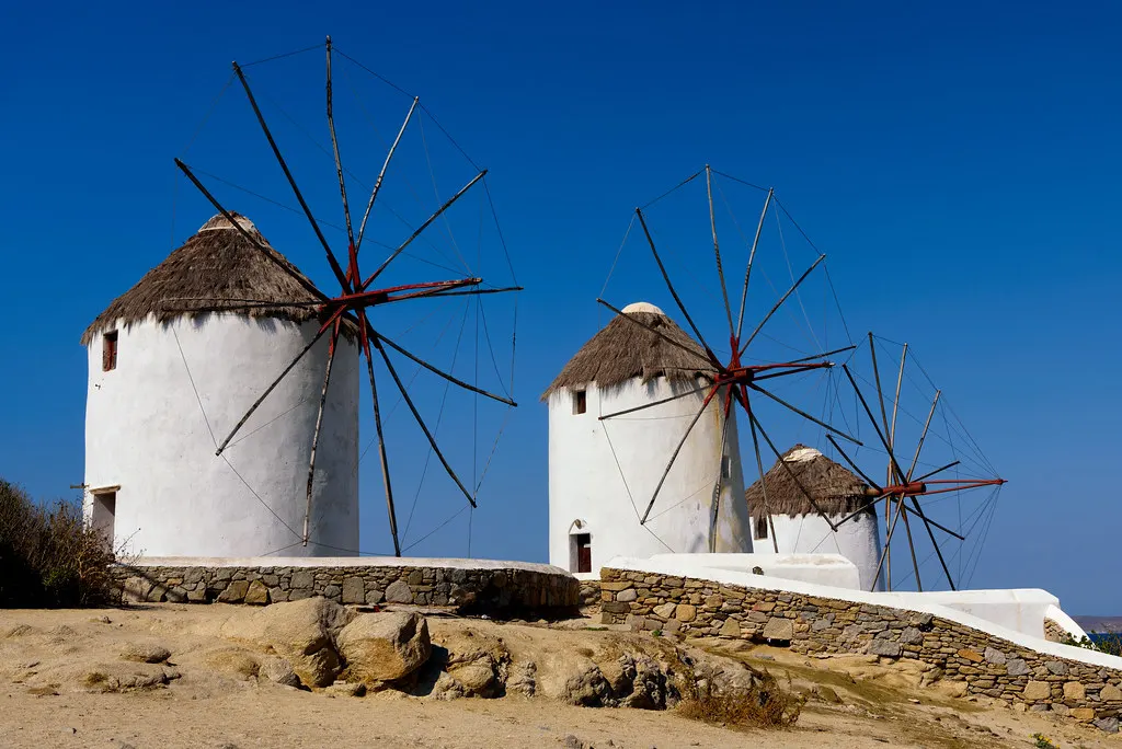 Witte windmolens met rieten daken en houten wieken op een heuvel onder een strakblauwe lucht op Mykonos