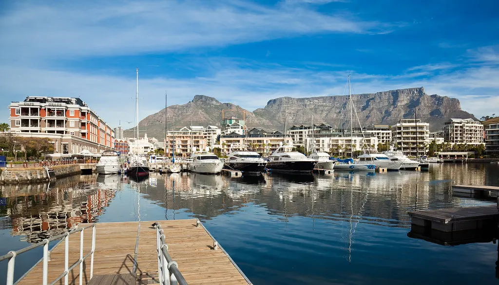 Jachthaven van de V&A Waterfront in Kaapstad met luxe boten en de Tafelberg op de achtergrond onder blauwe lucht