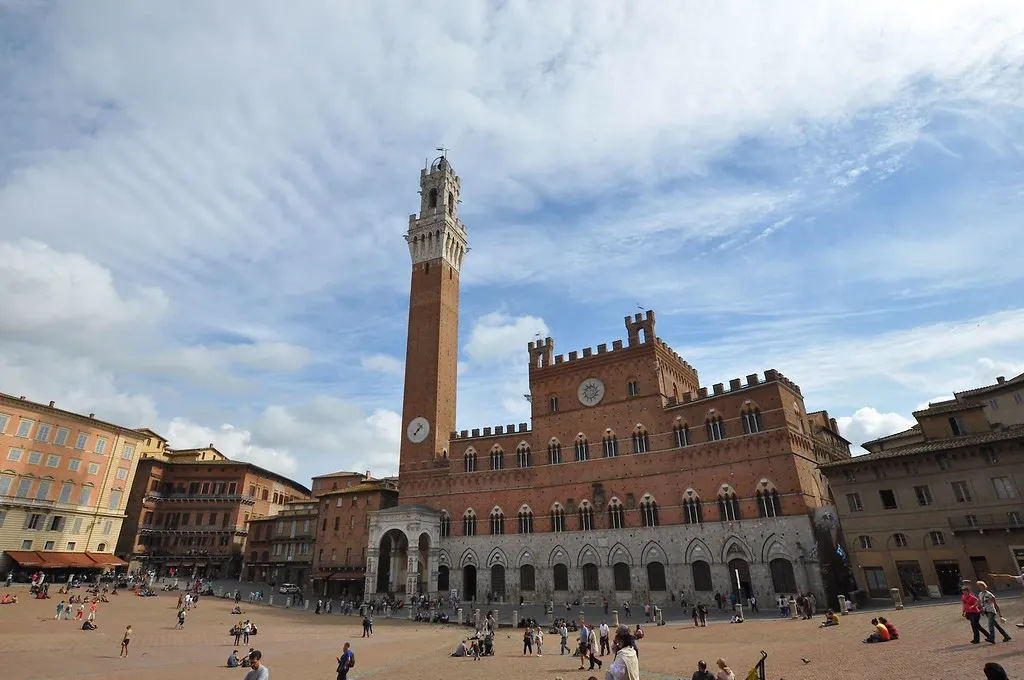Piazza del Campo in Siena met het Palazzo Pubblico en de Torre del Mangia onder een blauwe lucht