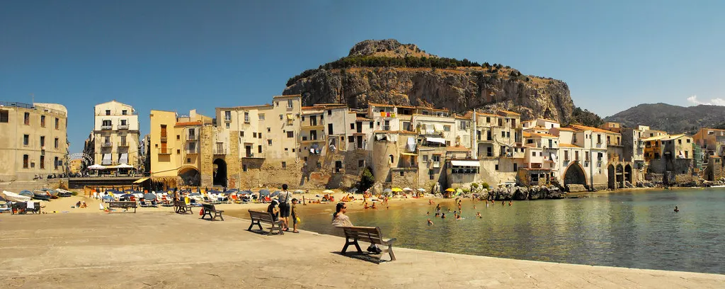 Strand van Cefalù met oude huizen aan het water en de rots La Rocca op de achtergrond