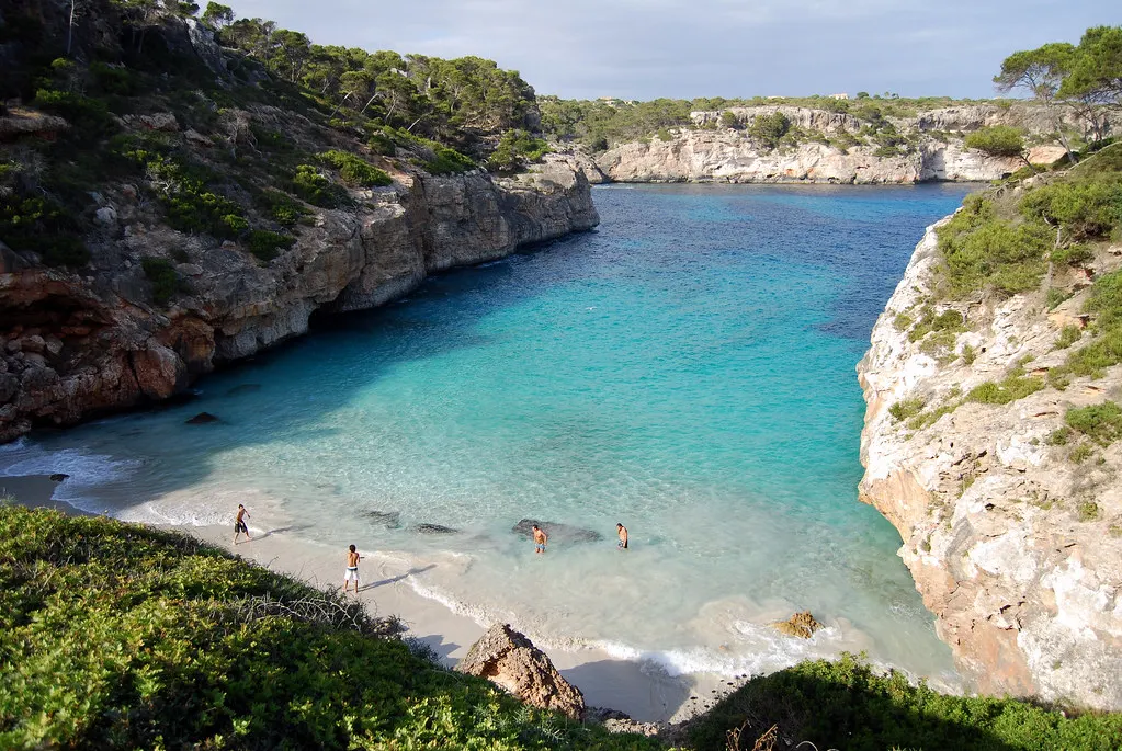 Smalle baai Es Caló des Moro met turquoise water tussen begroeide rotswanden en een klein zandstrand