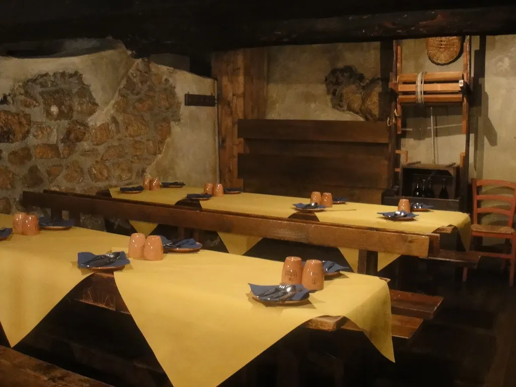 Rustieke restaurantzaal met lange houten tafels, gele tafelkleden en natuurstenen muur