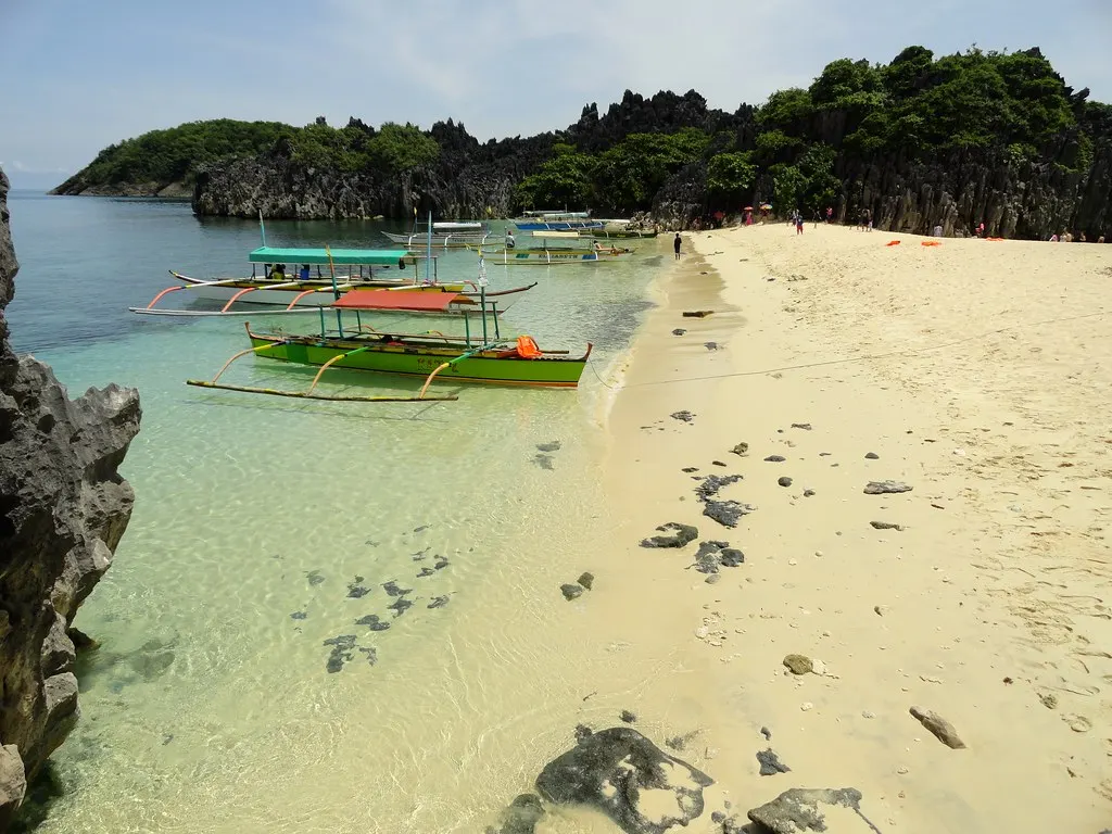 Wit zandstrand met helder water, bangka-boten en grillige kalkrotsen op Lahos Island in Caramoan