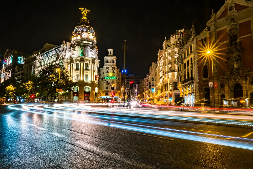 Gran Vía in Madrid bij nacht met het verlichte Metrópolis-gebouw en lichtsporen van verkeer