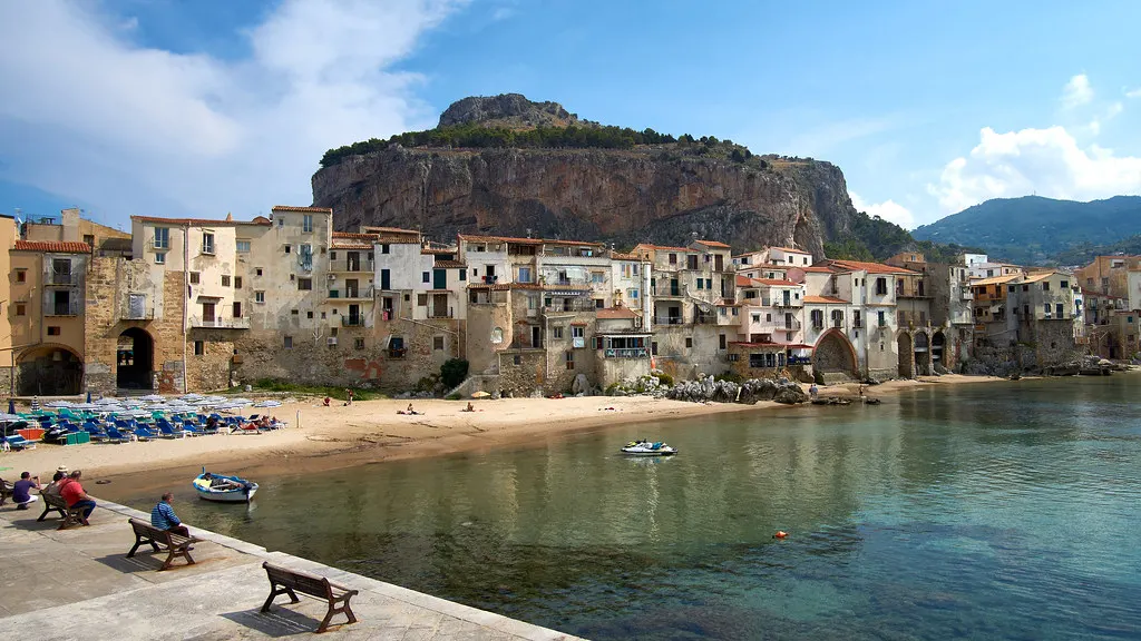 Strandje van Cefalù met oude huizen aan het water en de imposante rots La Rocca erachter