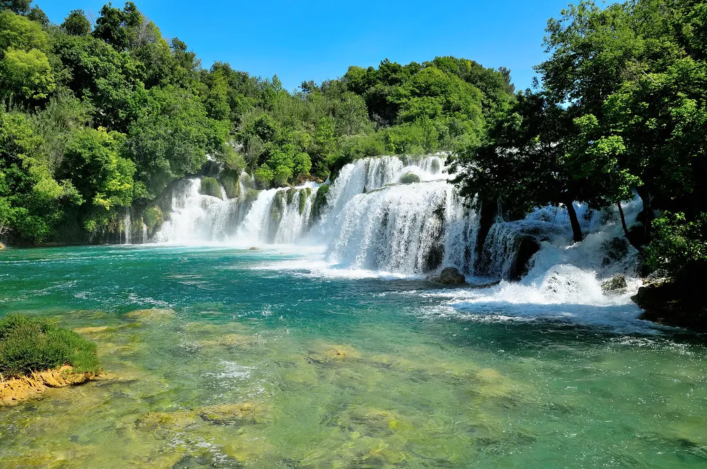 Brede cascade van de Skradinski Buk waterval met turquoise water en groene bomen onder een blauwe lucht