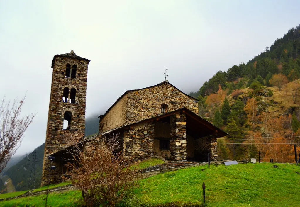Romaanse stenen kerk Sant Joan de Caselles met klokkentoren op een groene heuvel tussen herfstbergen