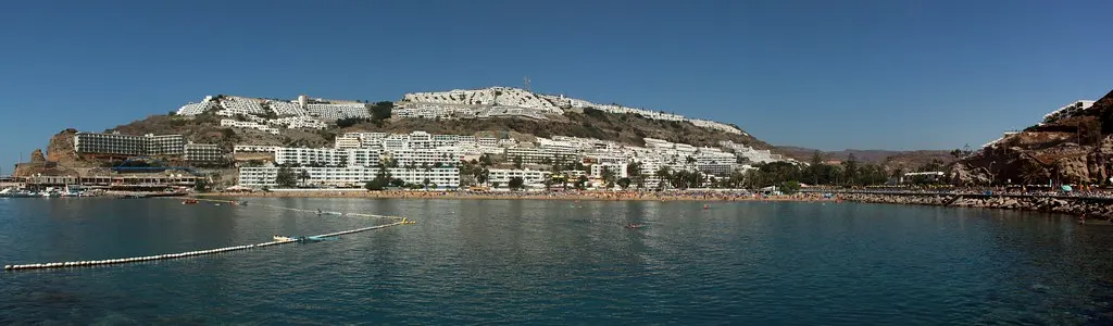 Panorama van de baai van Puerto Rico met kalm blauw water, strand en witte appartementen tegen de heuvels