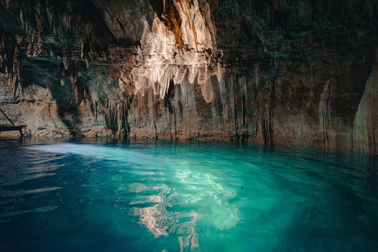 Turquoise water in een grotcenote met druipsteen, verlicht door zonlicht dat van boven naar binnen valt