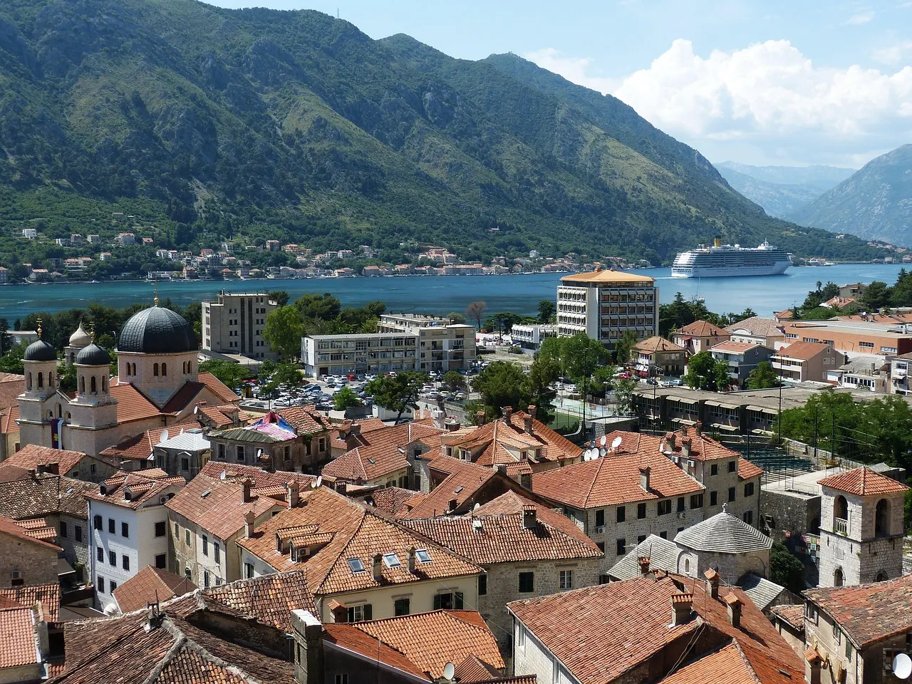 Uitzicht over de oranje daken van de oude stad Kotor op de baai, bergen en een cruiseschip