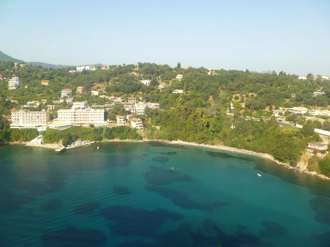 Groene heuvels met villa's en hotels boven een baai met helder turquoise water op Corfu