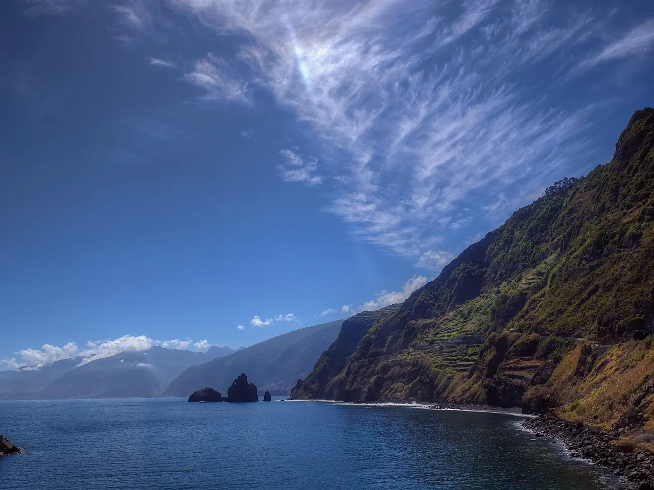 Groene steile kliffen langs de blauwe zee aan de noordkust van Madeira onder een heldere lucht