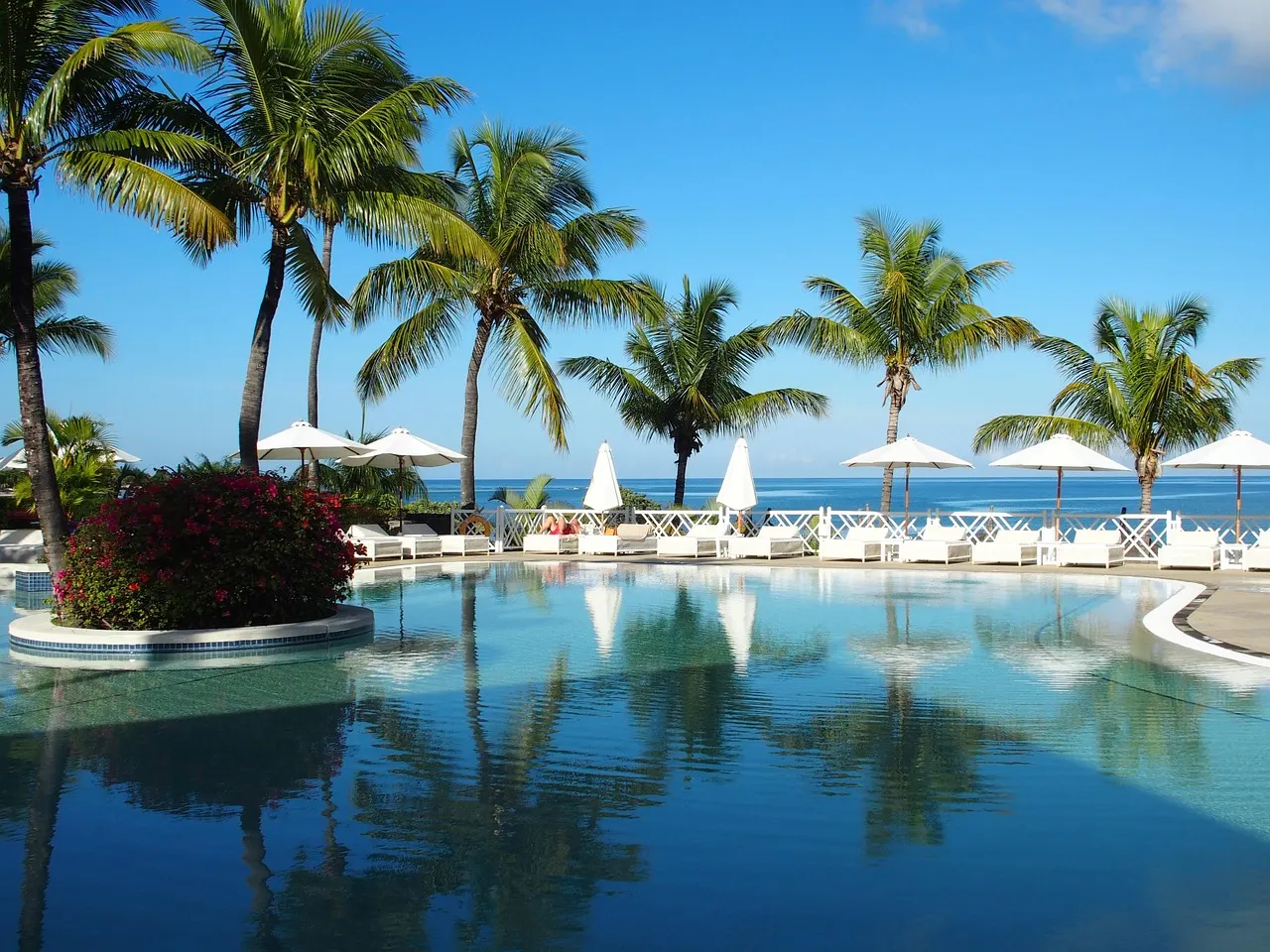 Zwembad met palmbomen, witte parasols en ligbedden aan zee bij een tropisch resort op Mauritius