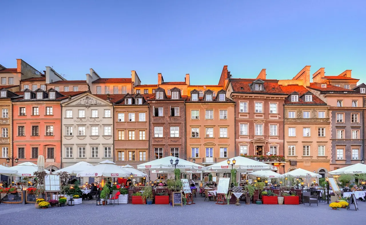 Kleurrijke gevels aan het Marktplein van de oude stad van Warschau met terrasjes onder een blauwe lucht