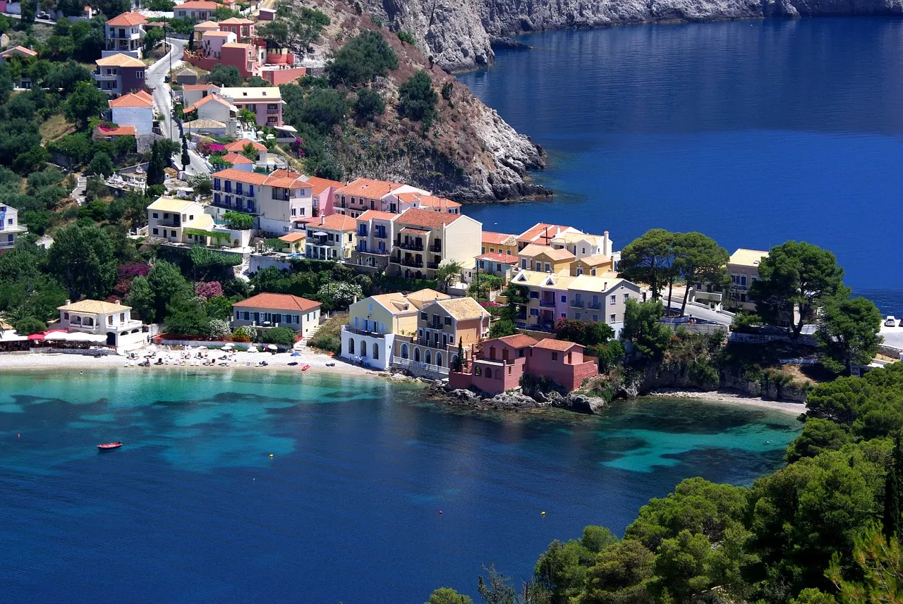 Kleurrijke huizen van het dorp Assos aan een turquoise baai, omringd door groene heuvels op Kefalonia
