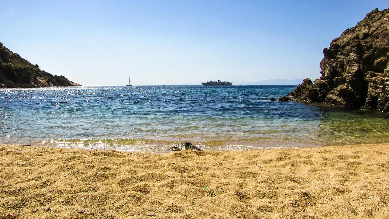Goudgeel zandstrand aan een heldere baai met rotsen en een schip op zee bij Skiathos