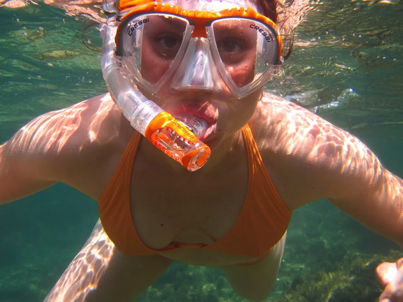 Snorkelaar met oranje duikbril en snorkel onder water in helder, zonovergoten zeewater