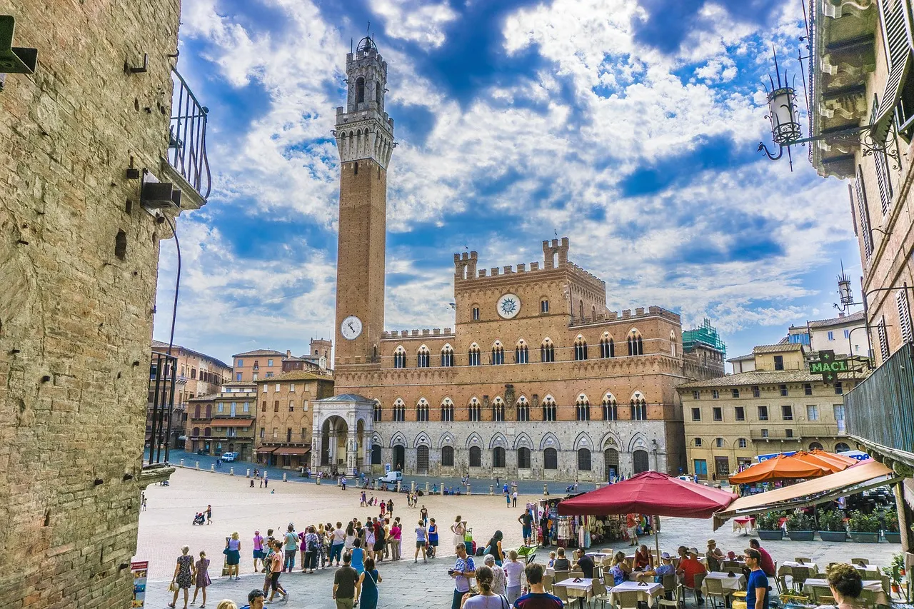 Piazza del Campo in Siena met het Palazzo Pubblico en de Torre del Mangia onder een blauwe lucht