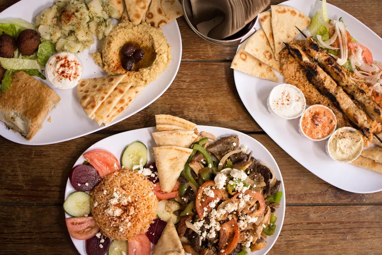 Tafel met meerdere borden Griekse gerechten: souvlaki, gyros met rijst, hummus, pitabrood en dips