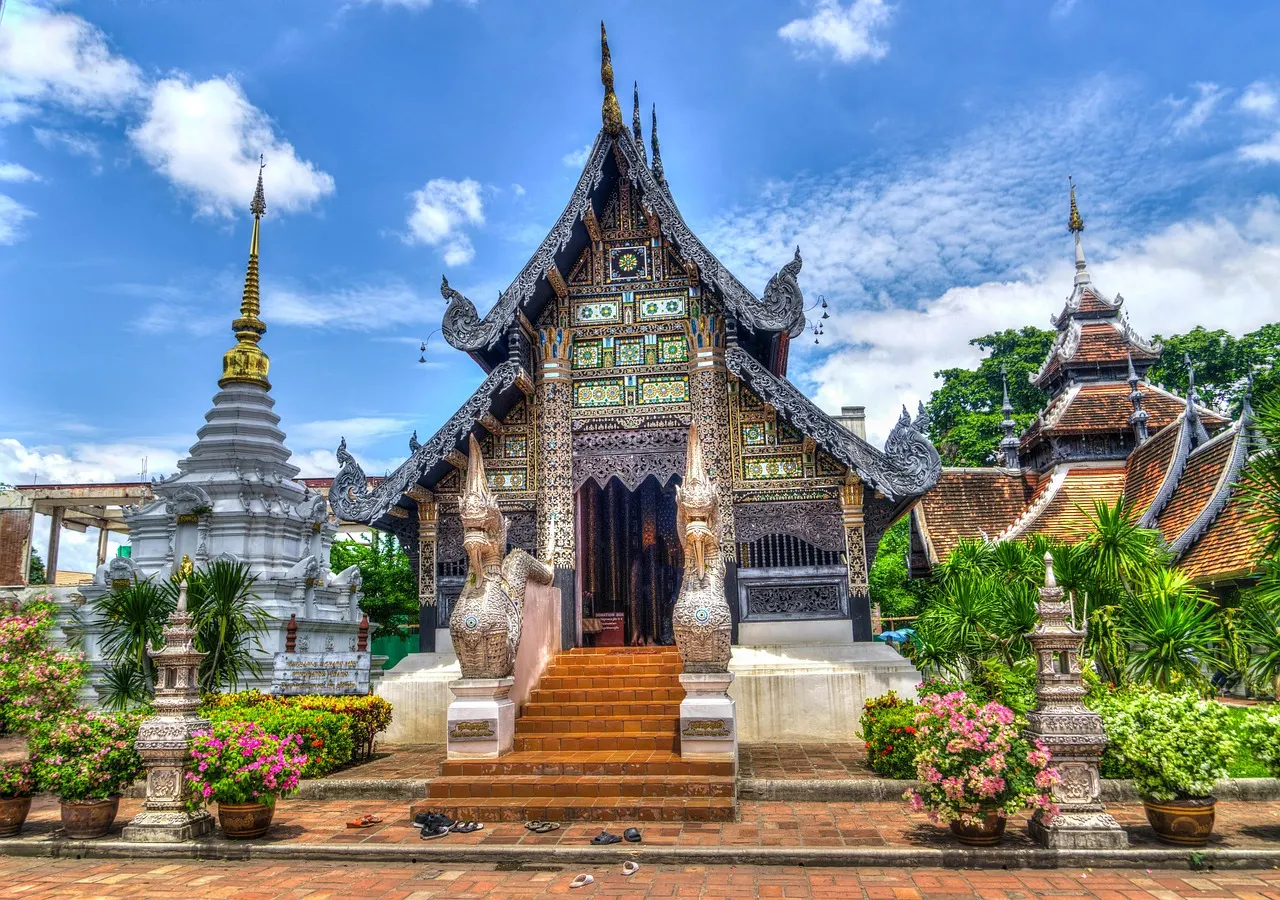 Sierlijke Thaise tempel met gouden versieringen, trappen met draakbeelden en een witte stoepa onder blauwe lucht