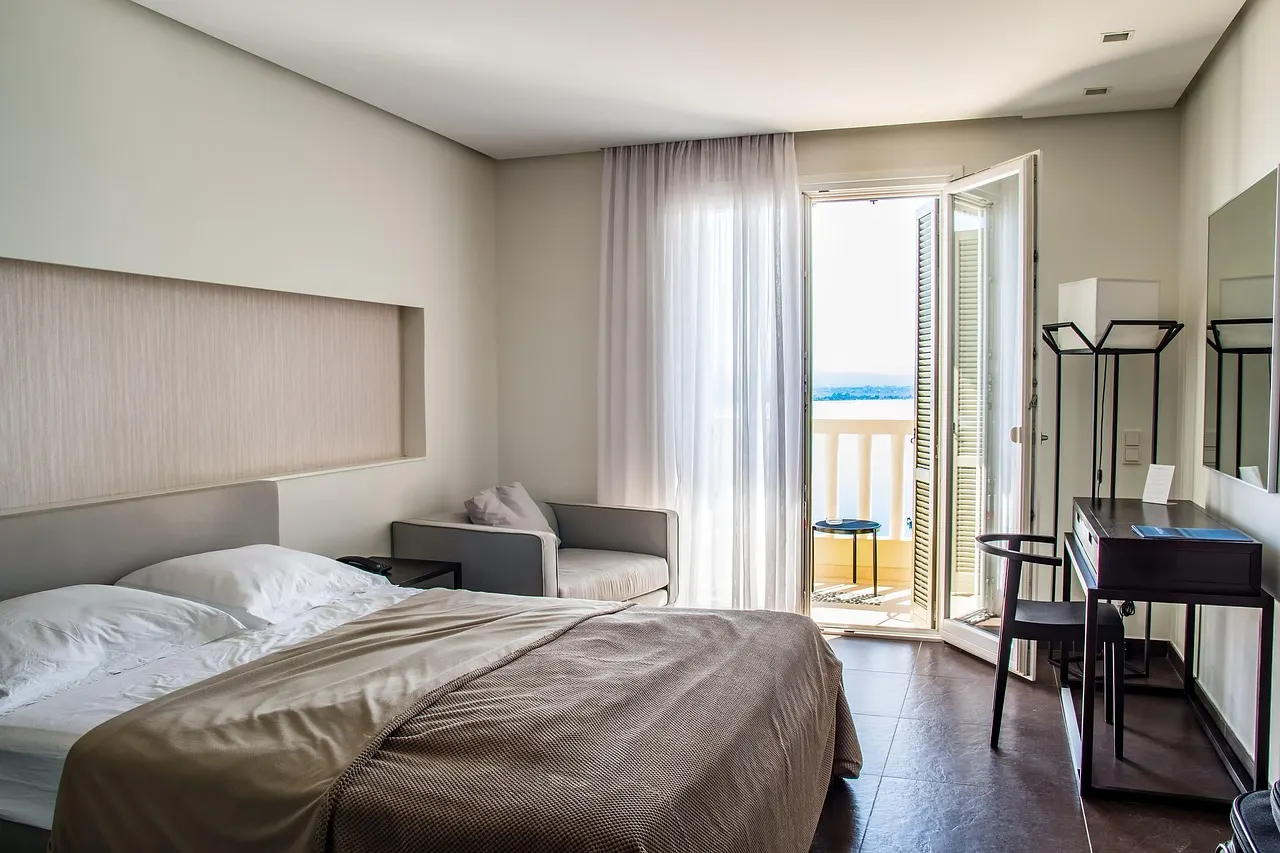 Lichte hotelkamer met tweepersoonsbed, fauteuil en openslaande deuren naar een balkon met zeezicht