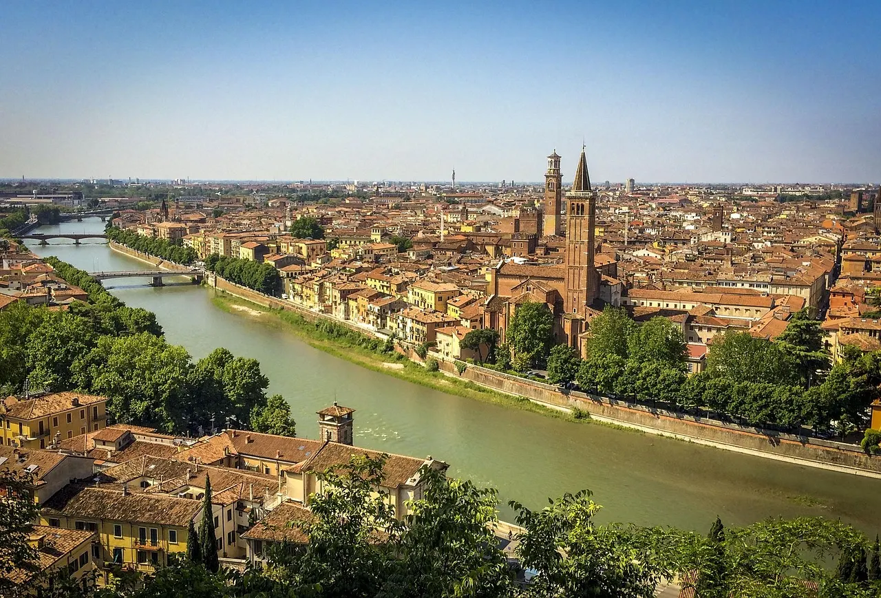 Panoramisch uitzicht over Verona met de groene rivier de Adige, rode daken en kerktorens onder een blauwe lucht