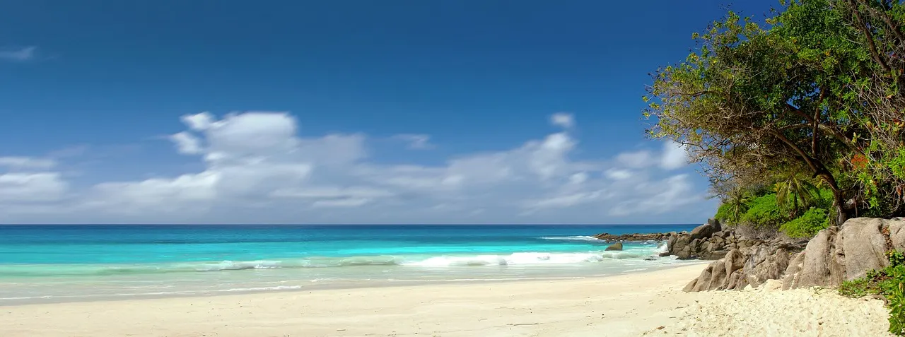 Wit zandstrand met turquoise zee, granietrotsen en tropisch groen onder een blauwe lucht op de Seychellen