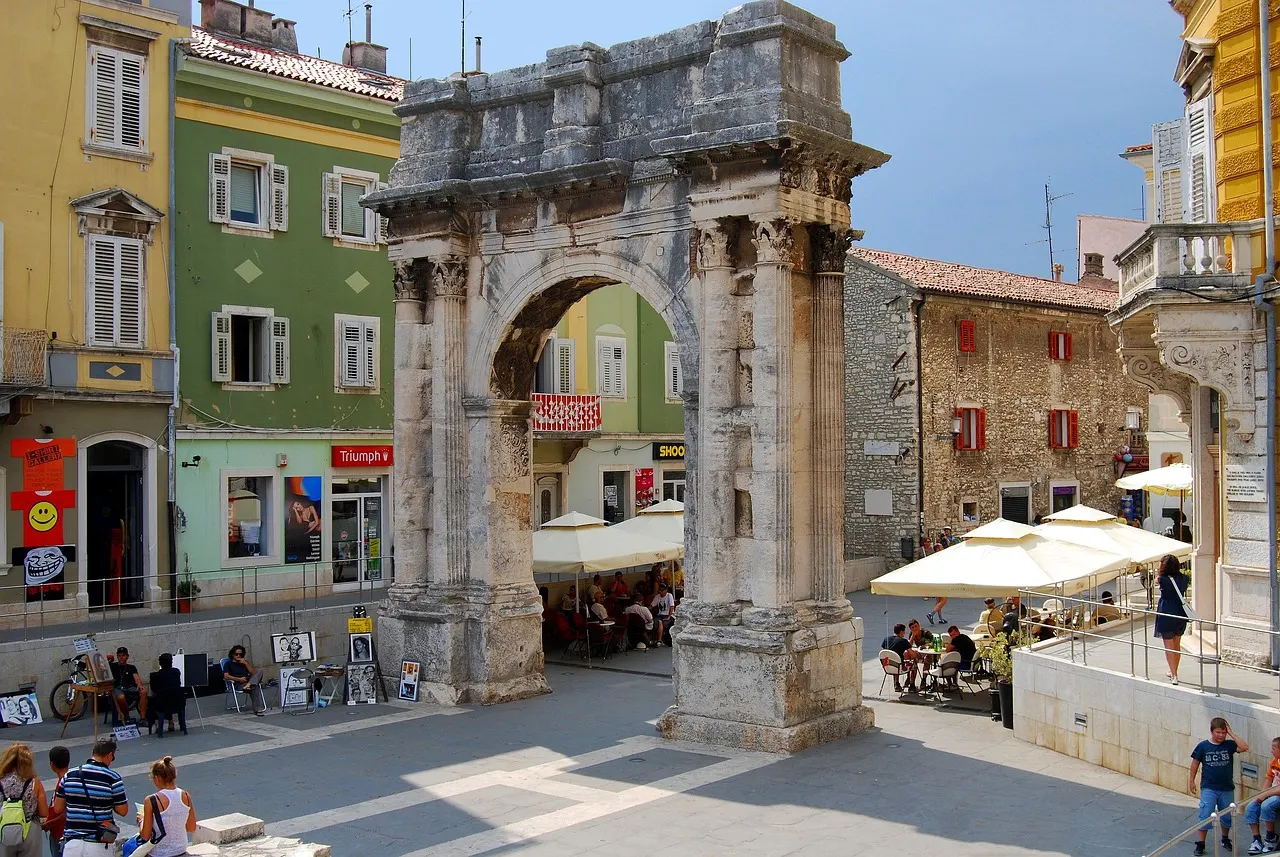 De Romeinse Boog van de Sergii in Pula met kleurrijke gevels en terrasjes eromheen onder een blauwe lucht