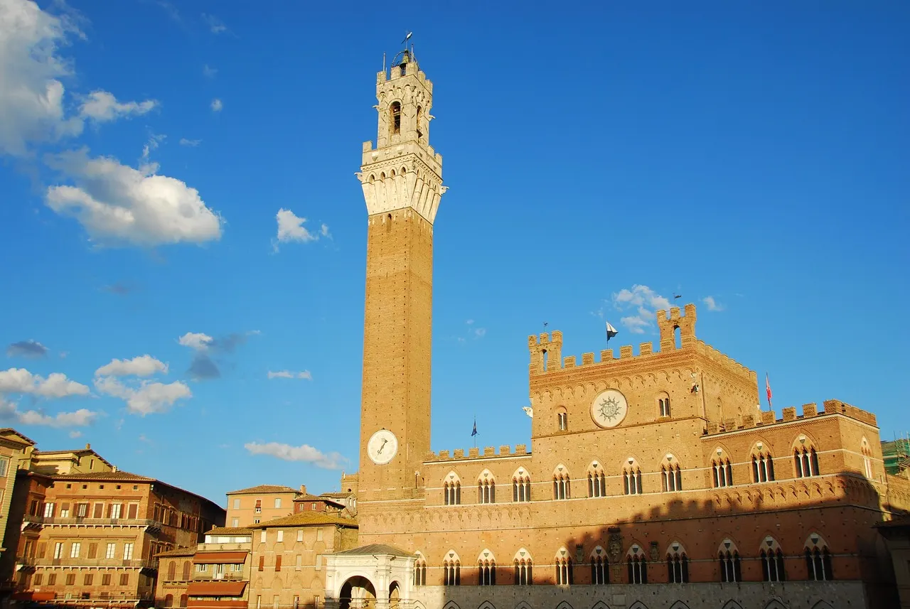 De Torre del Mangia naast het Palazzo Pubblico aan de Piazza del Campo in Siena onder een blauwe lucht