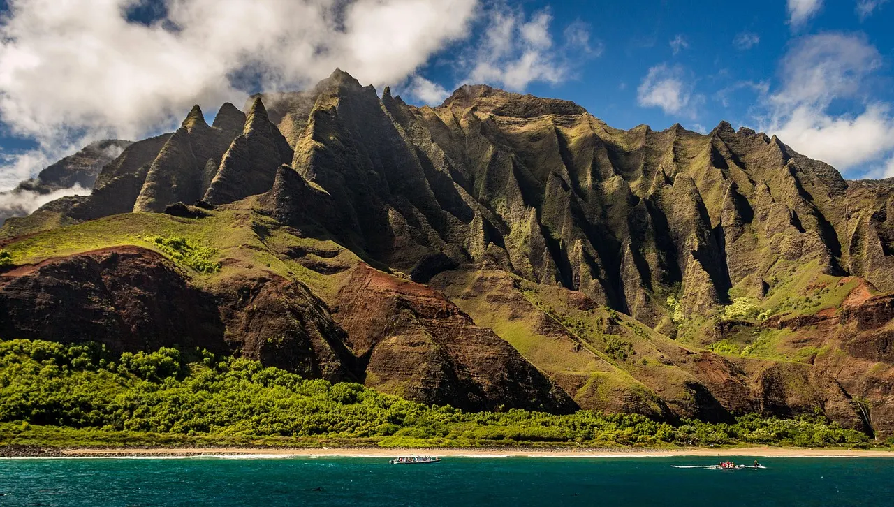Gekartelde groene kliffen van de Na Pali-kust boven een strand en turquoise zee op Kauai