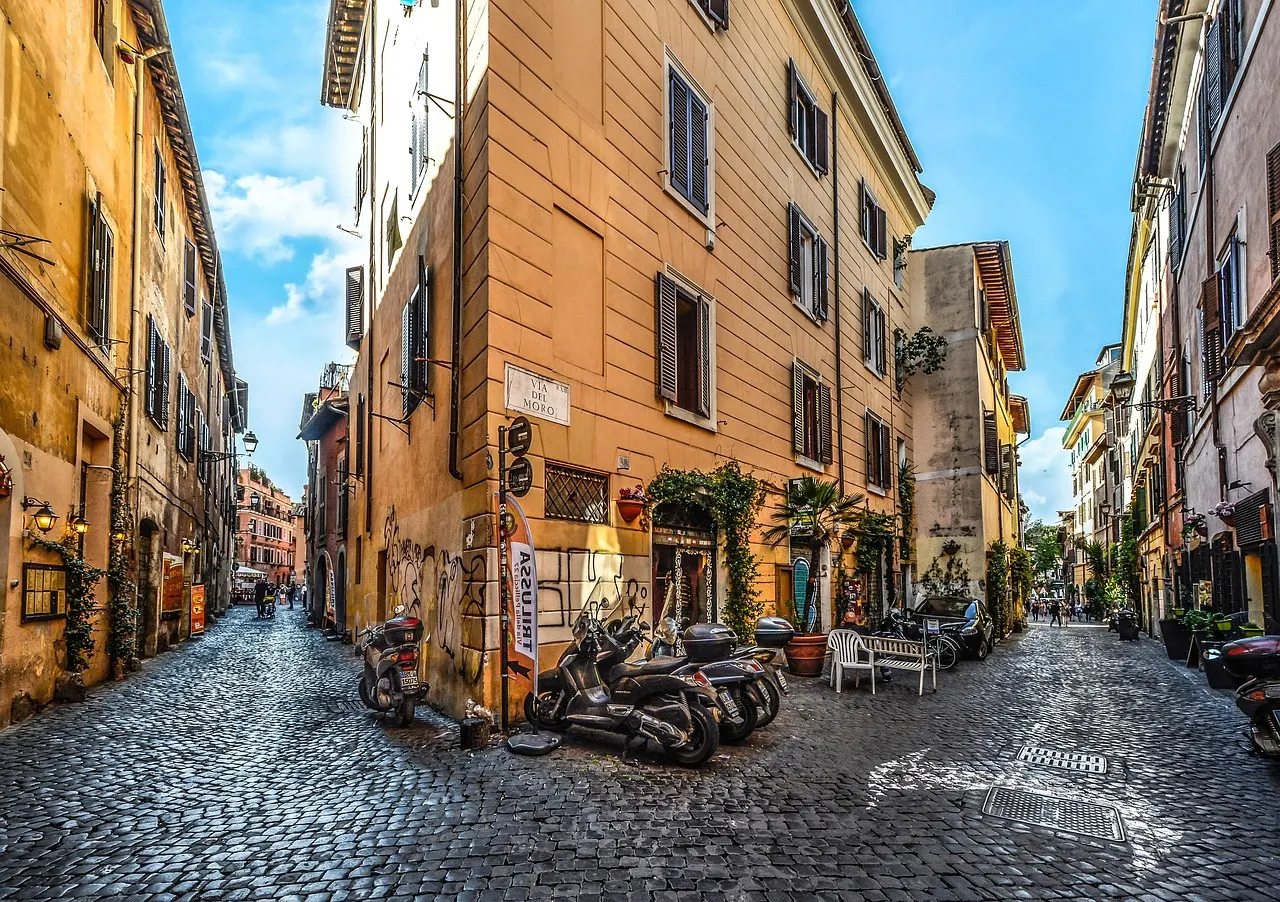 Zonnige geplaveide straat in Trastevere met okerkleurige gebouwen, scooters en planten