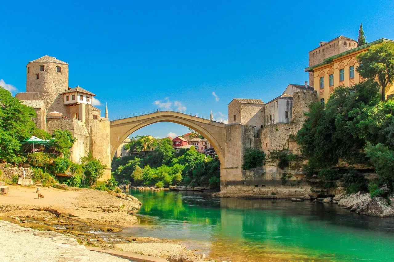 De Oude Brug van Mostar met stenen torens boven de groenblauwe rivier Neretva onder een strakblauwe lucht