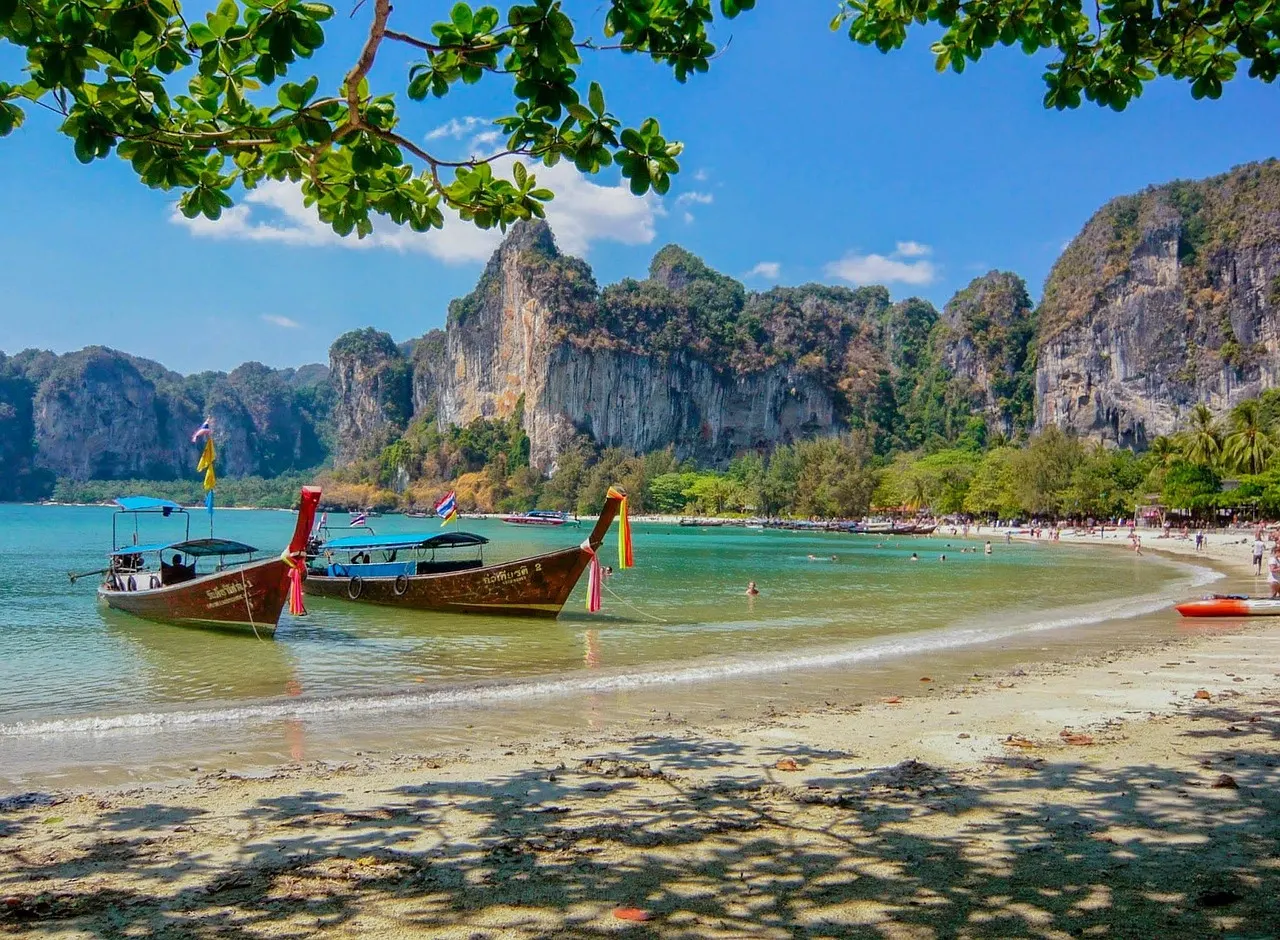 Longtailboten op een tropisch zandstrand met turquoise water en kalkstenen rotsen, Railay Beach in Thailand
