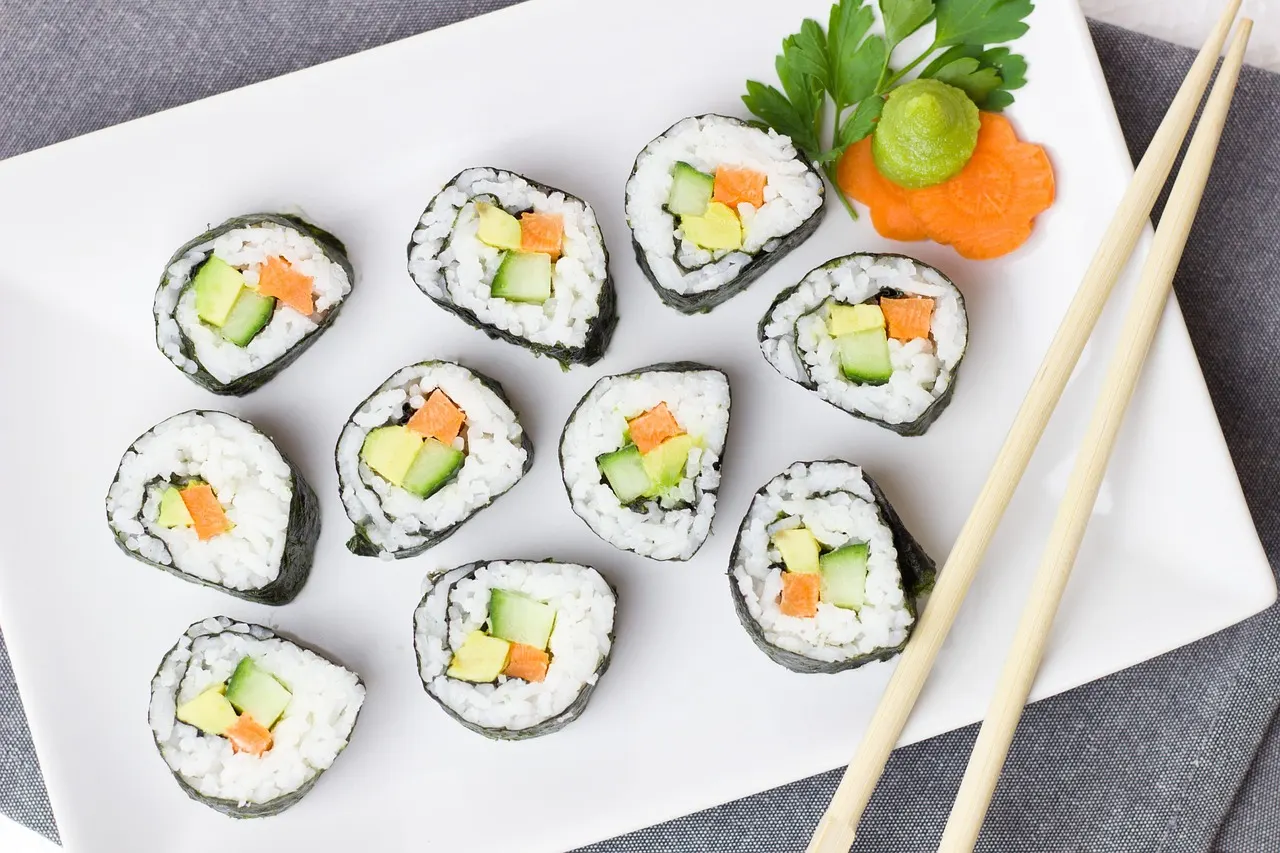 Wit bord met maki-sushi gevuld met komkommer, wortel en avocado, met wasabi en eetstokjes