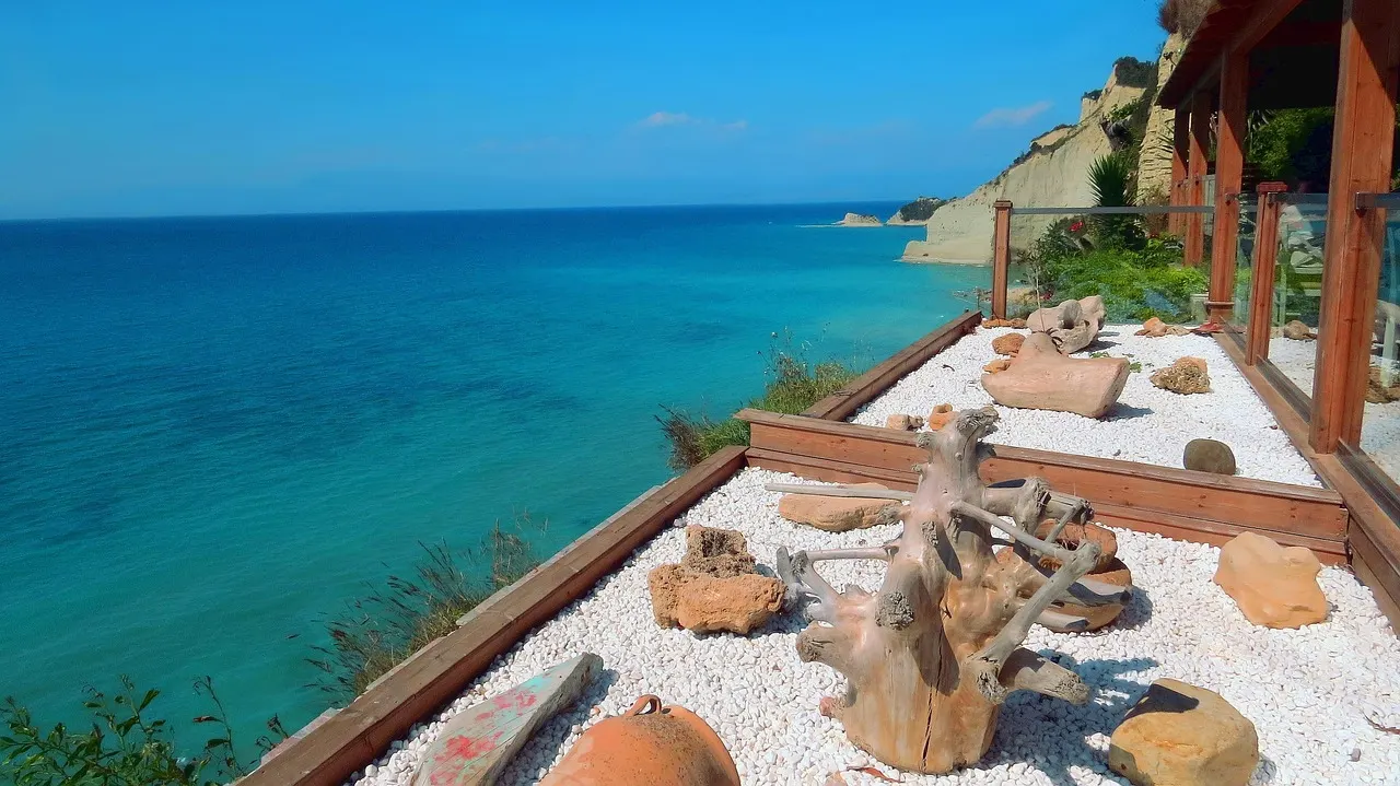Turquoise zee langs de kliffen van Corfu, gezien vanaf een terras met witte kiezels en drijfhout