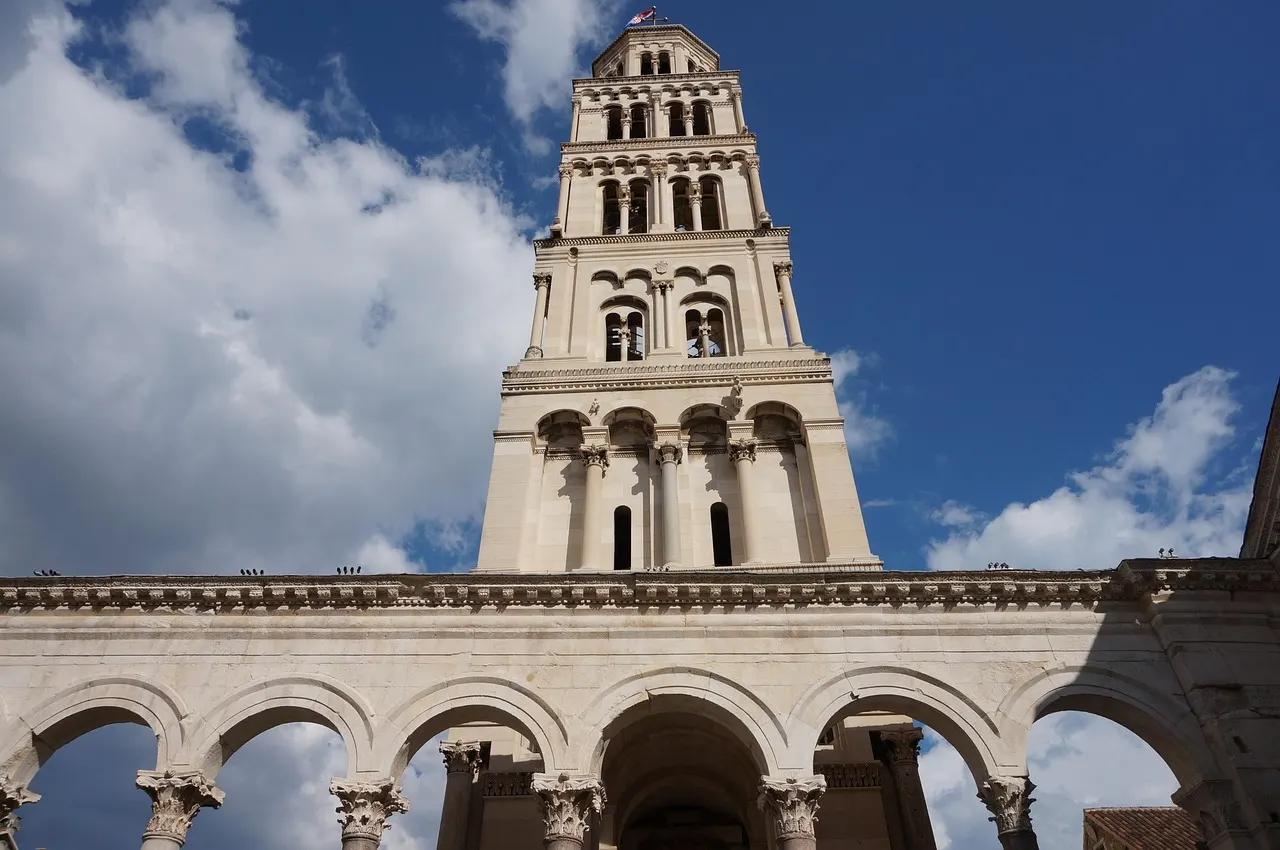 De witte klokkentoren van de kathedraal van Split boven de zuilengalerij van het Peristilium, tegen een blauwe lucht