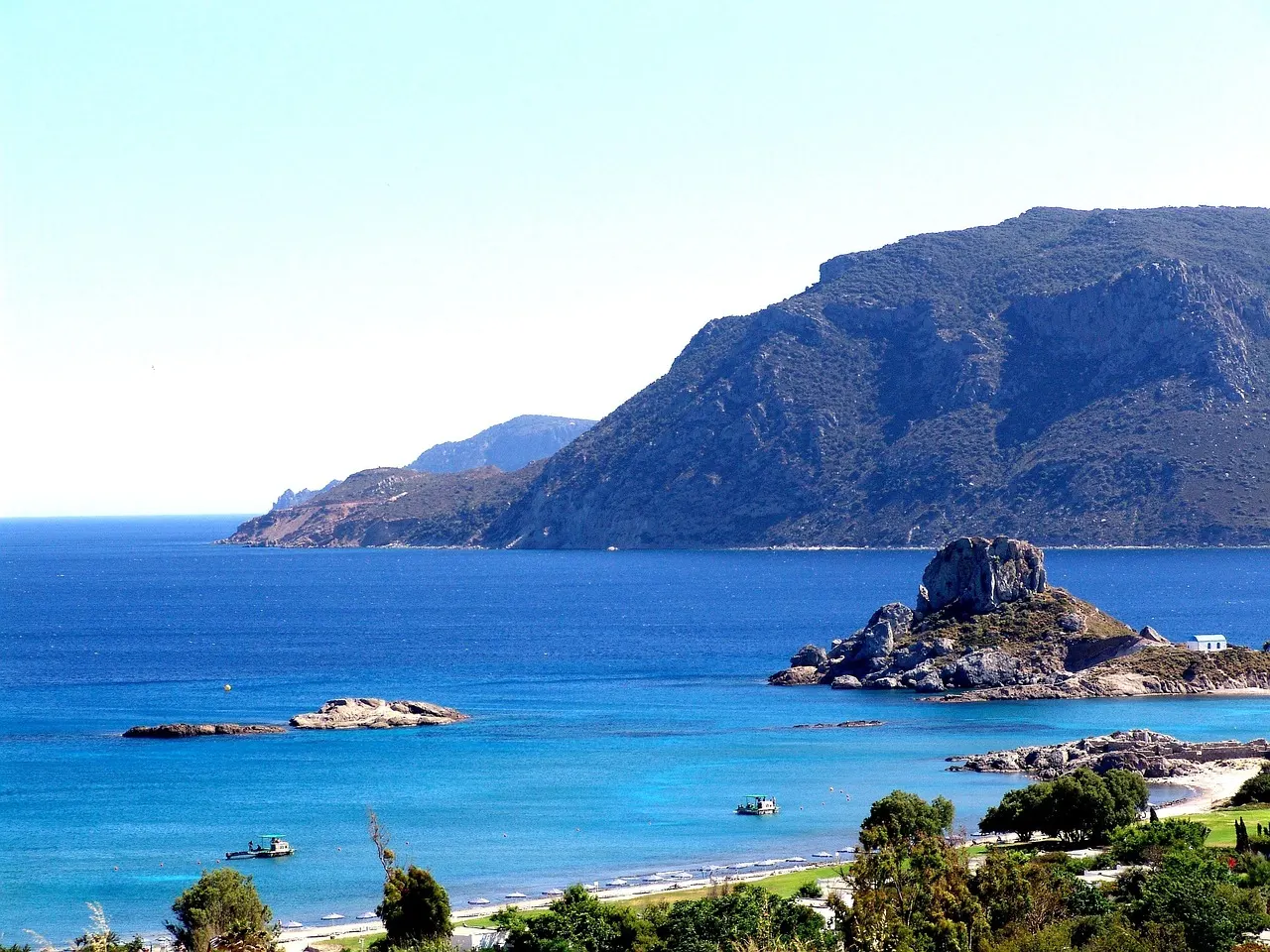 Baai van Kefalos op Kos met blauw water, strand en het rotseilandje Kastri met kapel